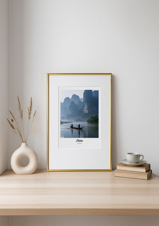 Framed artwork on a shelf with a vase, books, and a cup.