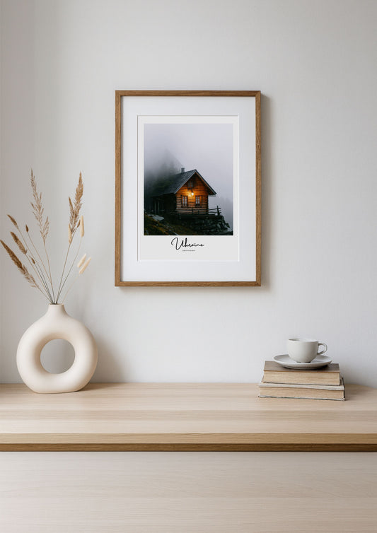 Framed photograph of a cabin in the woods on a wooden shelf with decor items.