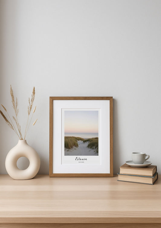 Framed artwork on a wooden shelf with a vase and books against a white wall