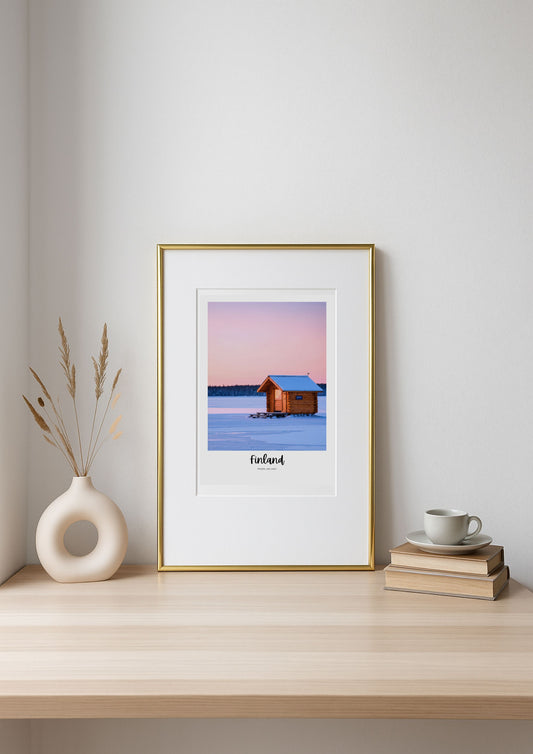 Framed artwork of a cabin in a snowy landscape on a shelf with decor items.