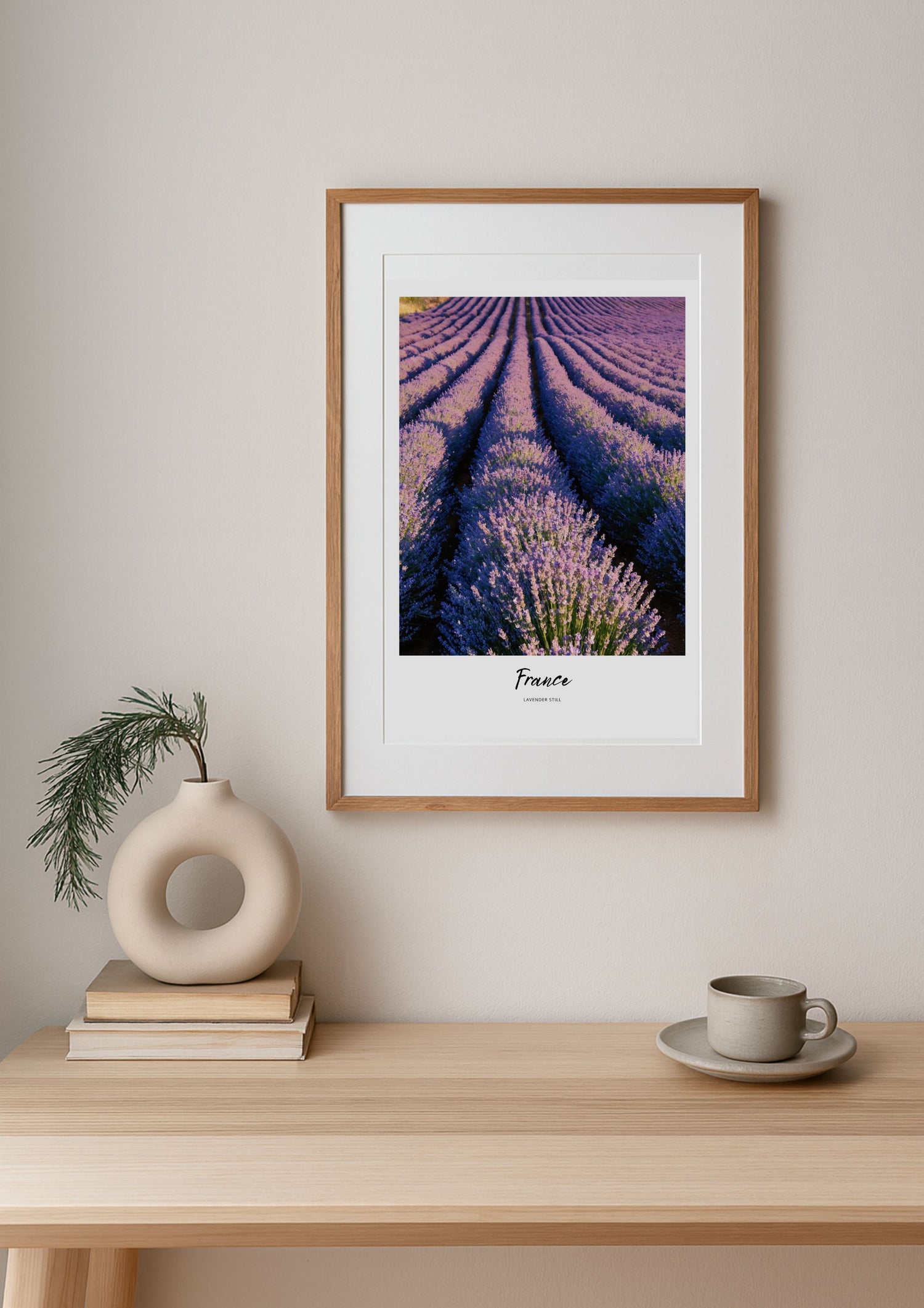 Framed artwork of lavender fields on a wall above a wooden table with decor items.
