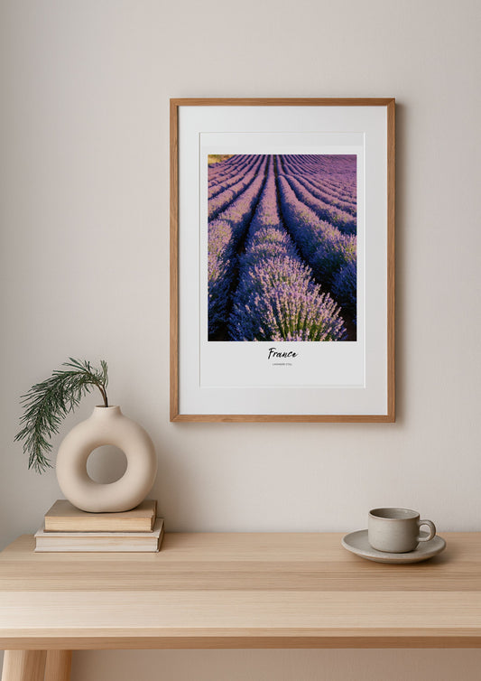 Framed artwork of lavender fields on a wall above a wooden table with decor items.