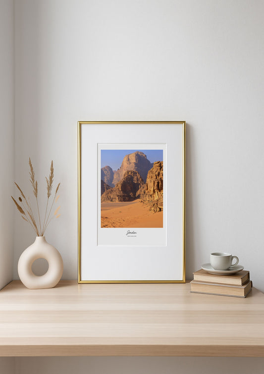 Framed desert landscape print on a wooden shelf with decor items.