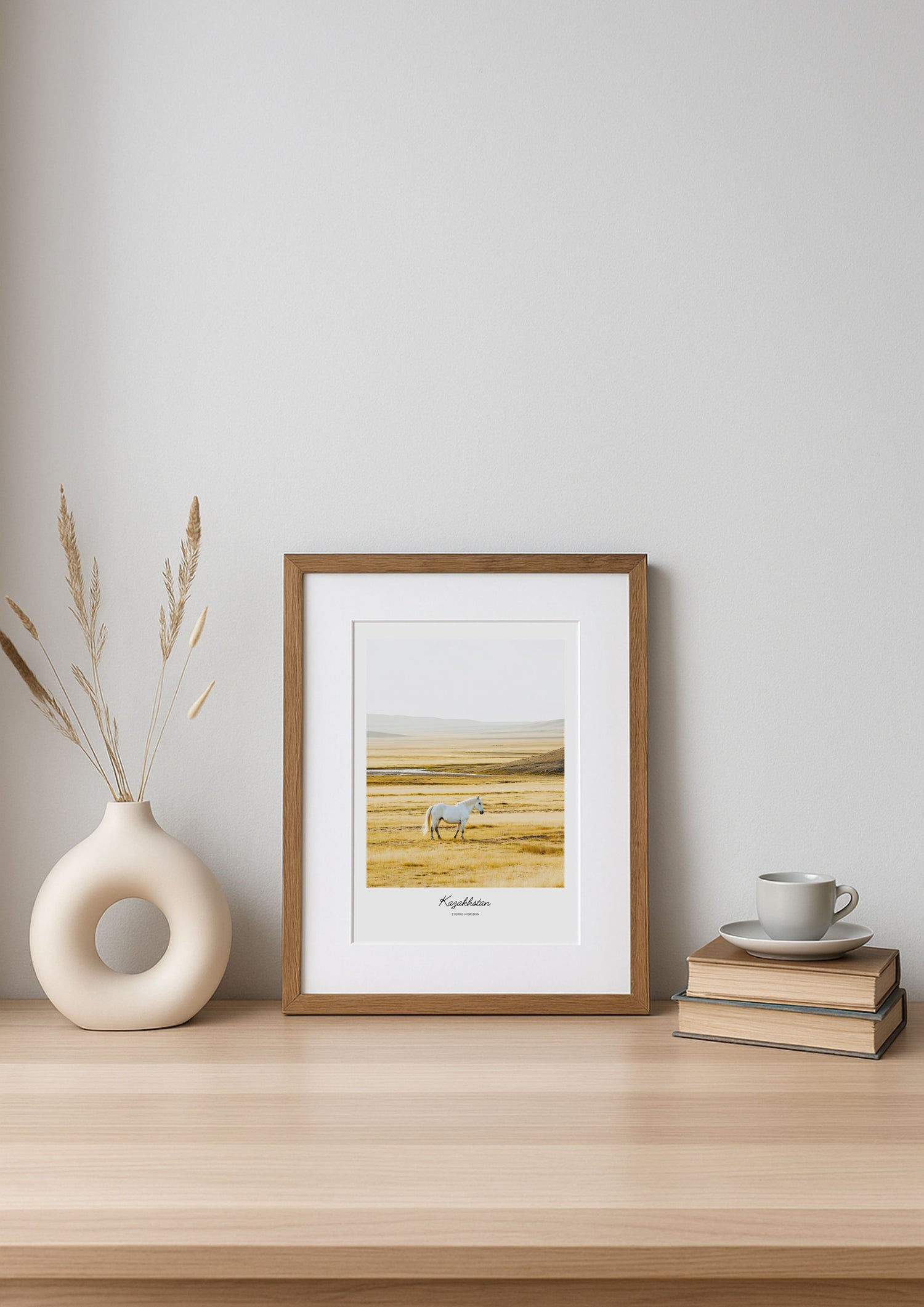 Framed artwork of a landscape with a deer on a wooden shelf against a white wall.