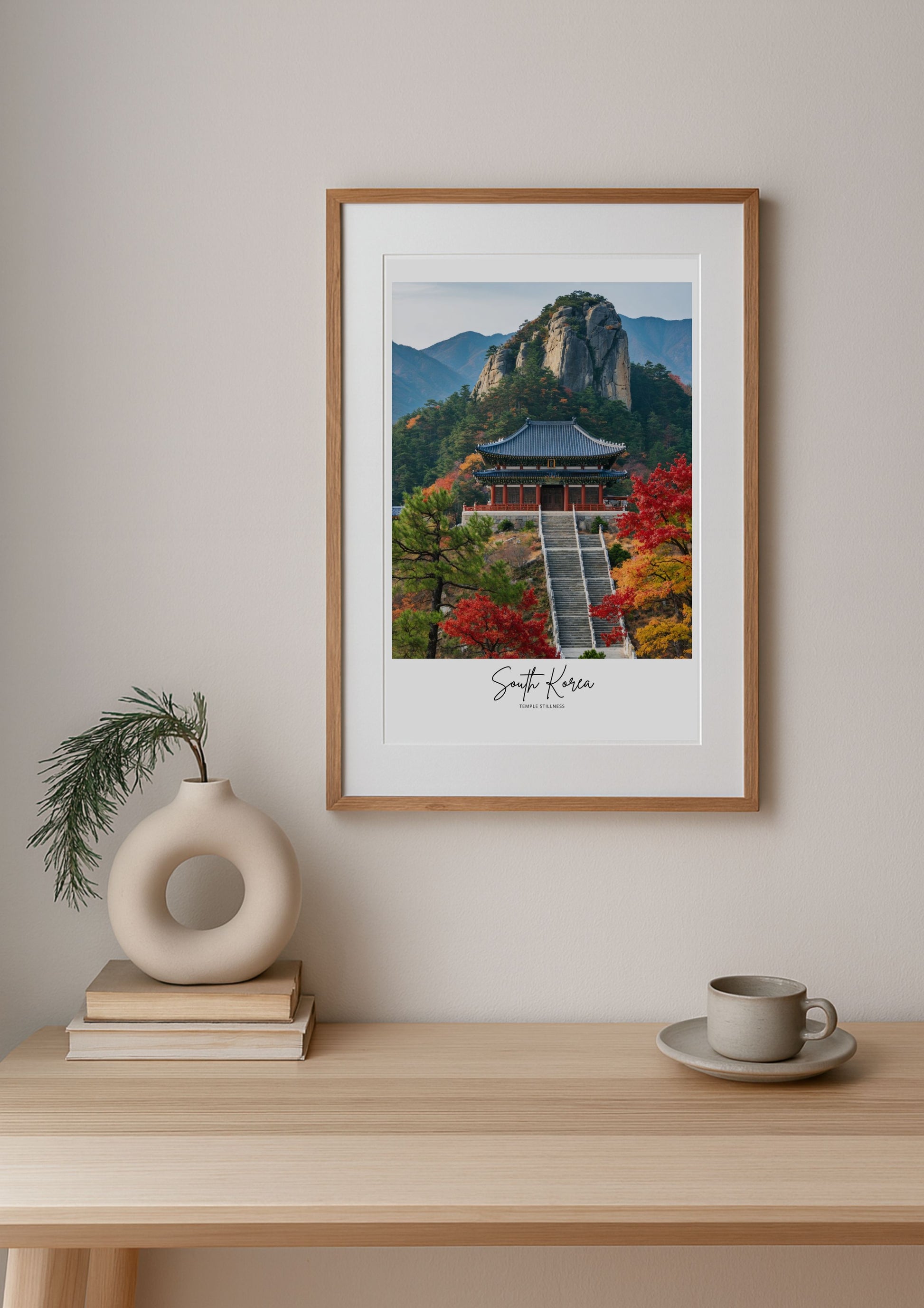 Framed print of a scenic landscape with a building and mountains on a wall above a wooden table.