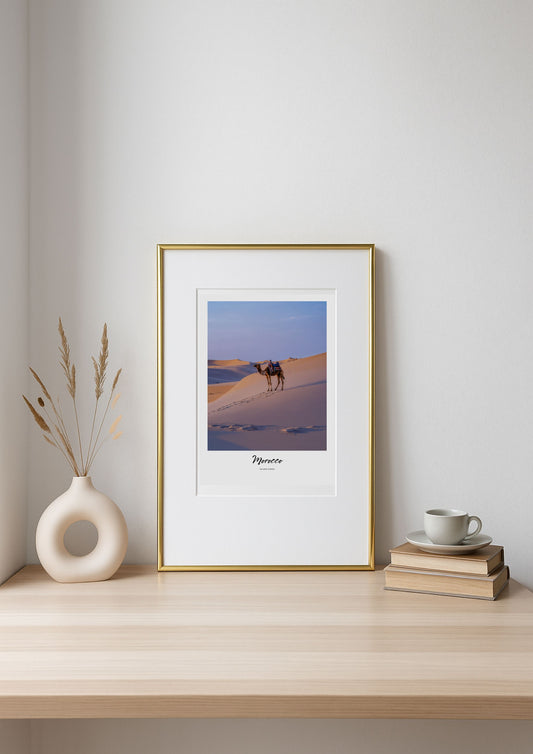 Framed artwork of a desert scene with camels on a shelf.