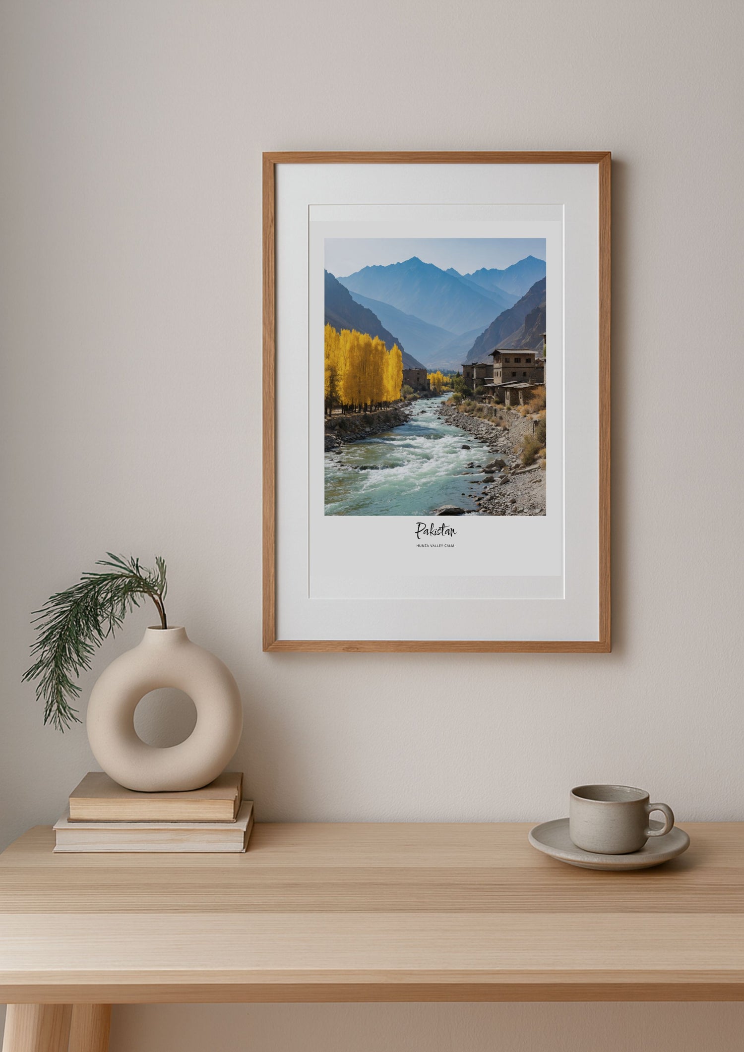 Framed artwork of a mountain landscape with trees on a wall above a wooden table.