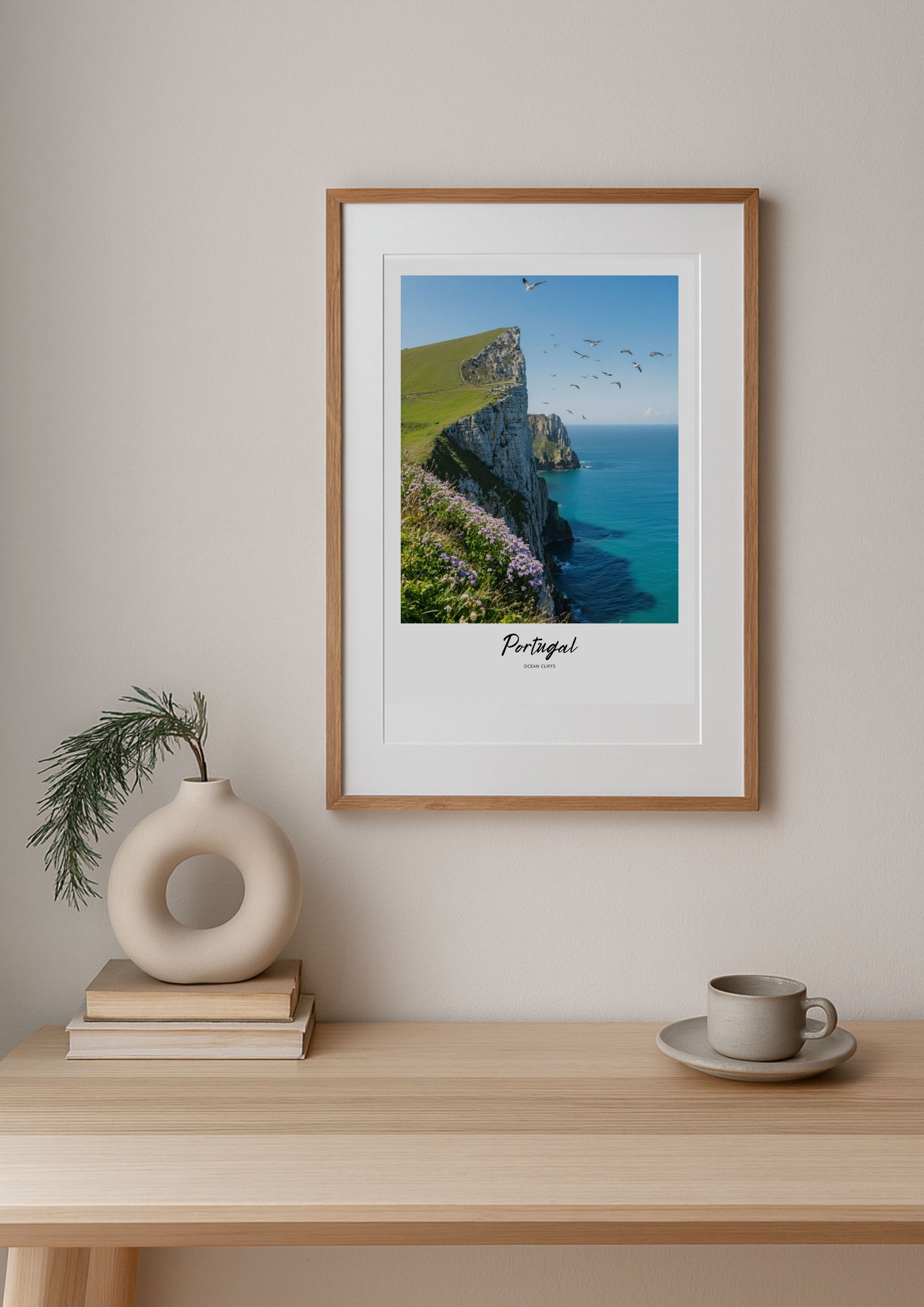 Framed artwork of a coastal scene with cliffs and sea, placed on a wall above a wooden table with decor items.