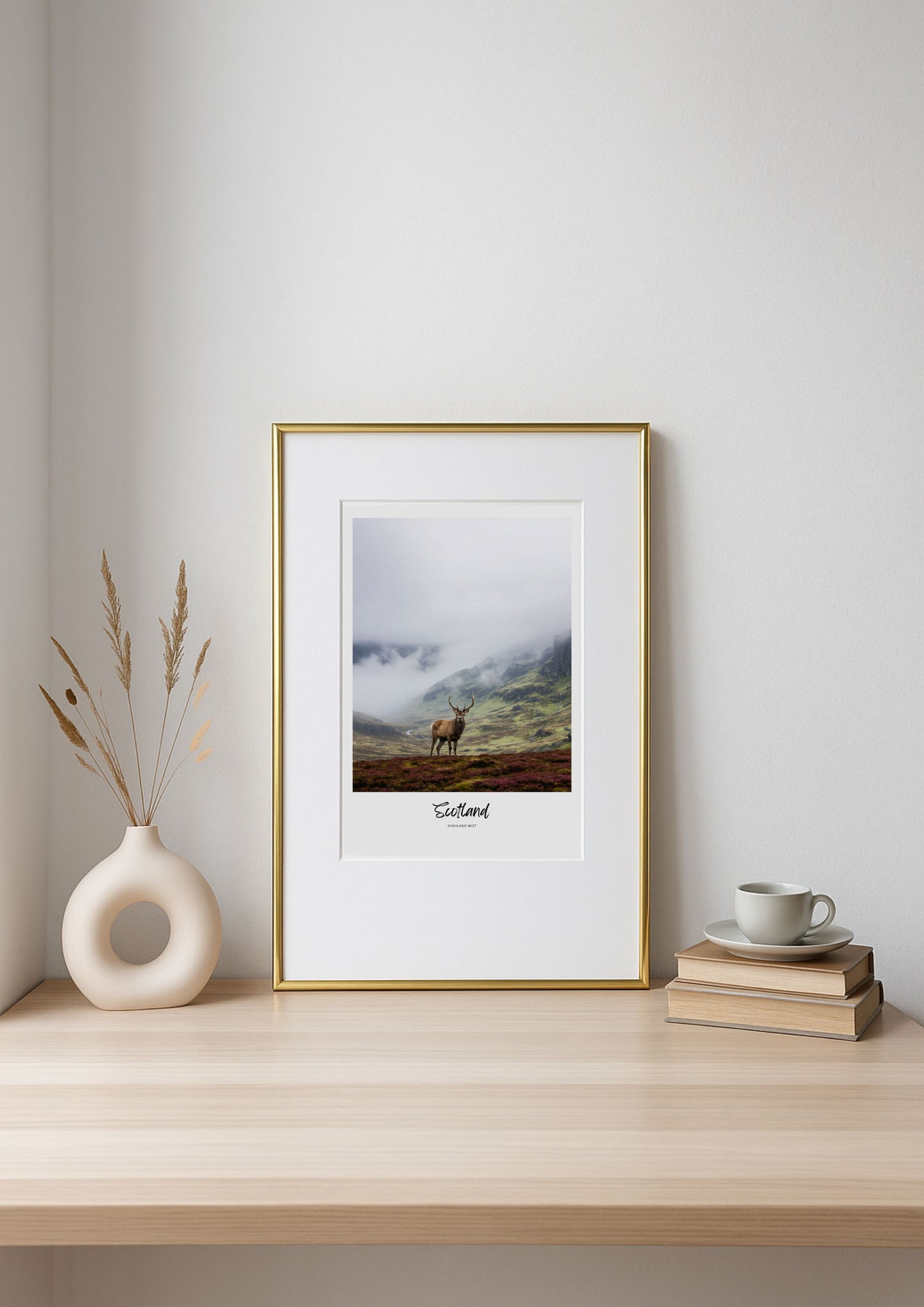 Framed print of a deer in a mountainous landscape on a shelf with decor items.