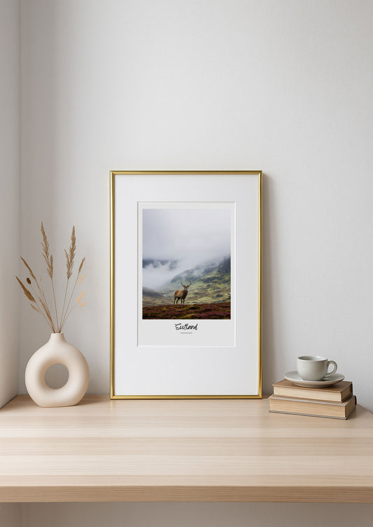 Framed print of a deer in a mountainous landscape on a shelf with decor items.