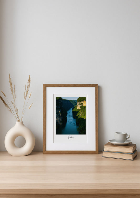Framed artwork on a wooden shelf with a vase and books in the background