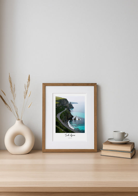 Framed artwork of a coastal scene on a wooden shelf with a vase and books.
