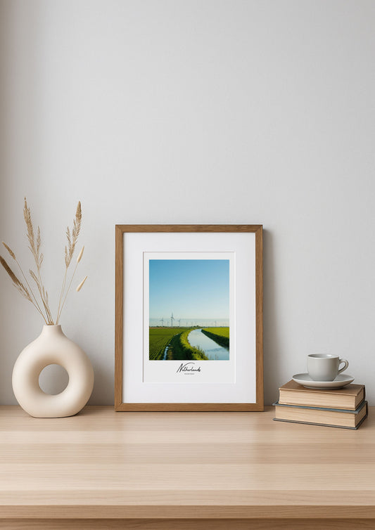 Framed artwork on a wooden shelf with a vase and books against a white wall