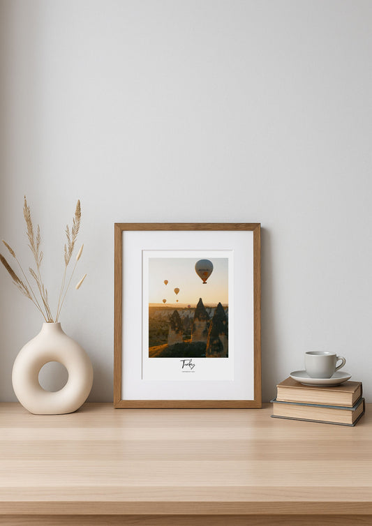 Framed artwork on a wooden shelf with a vase and books against a white wall
